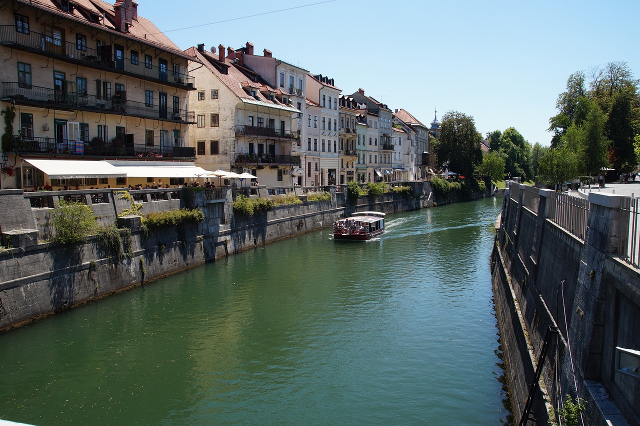 Blick auf die Ljubljanica in Ljubljana. Ein Boot fährt auf dem Fluss zwischen charmanten Häusern.